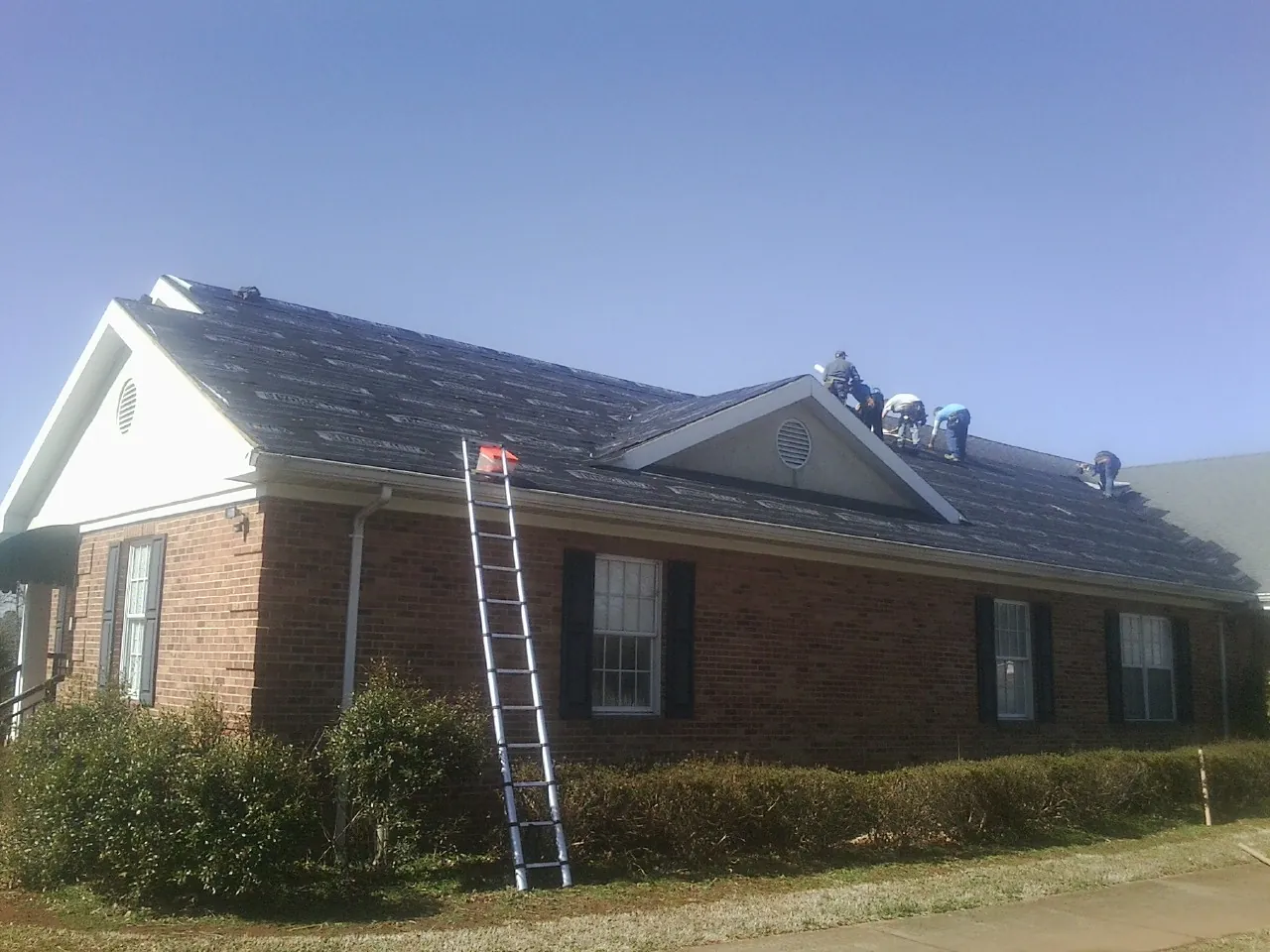 Crew tearing shingles off a brick ranch roof with a ladder set — Emergency Roof Repair work by our crew in Hebo