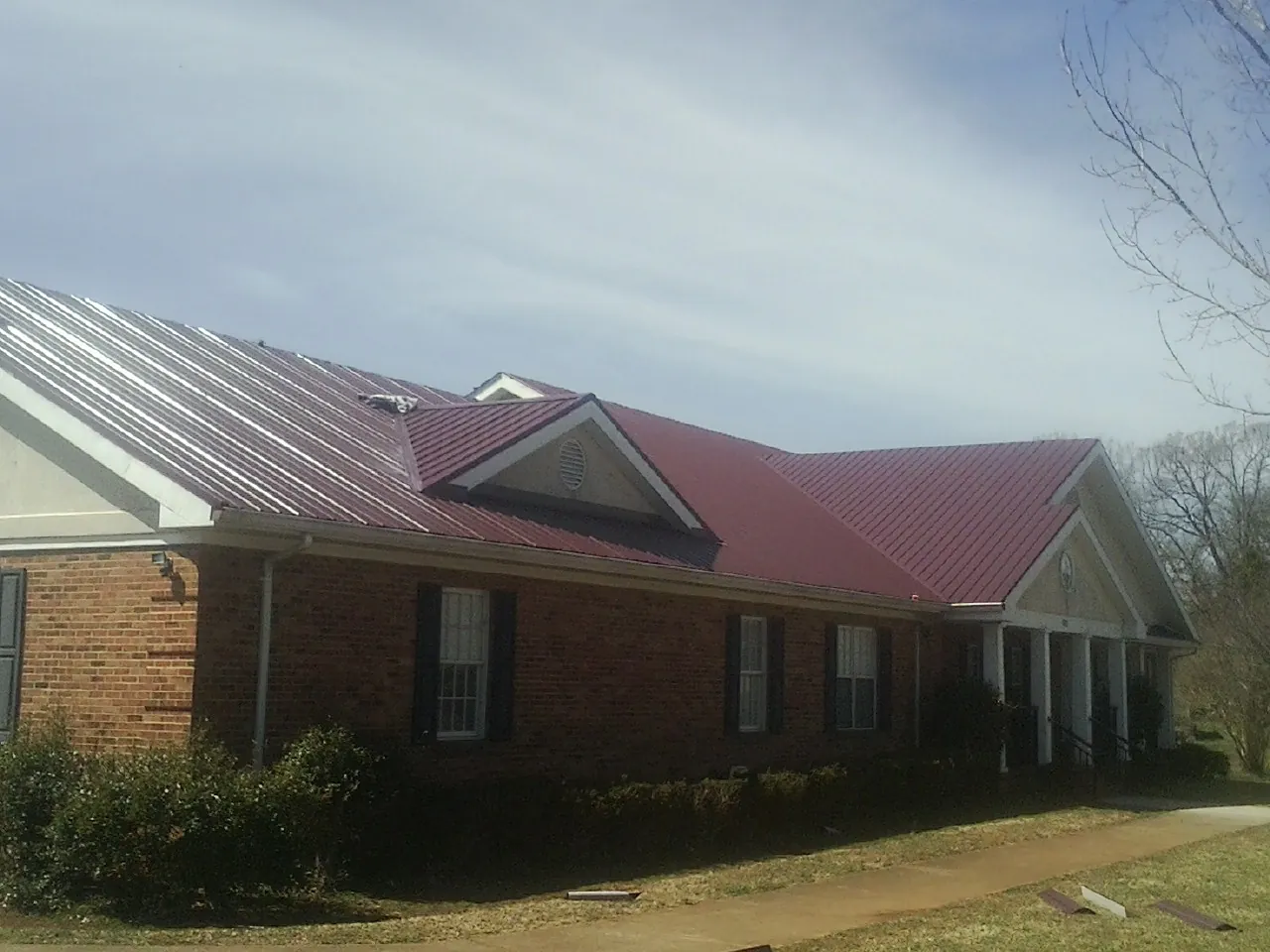 Red metal roof with gabled entries on a long brick building, from a Hail Damage Roof Repair job in Hebo