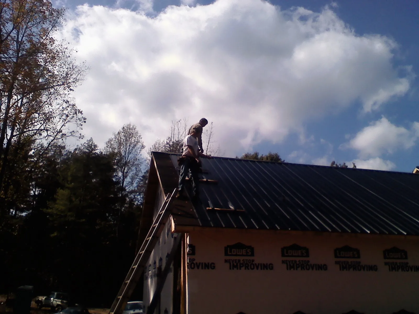 Roofer fastening dark metal panels high against a cloudy sky, from a Roof Inspection job in Hebo