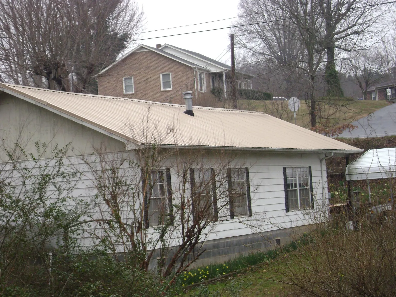 Tan metal roof on a white sided house set into a hillside — Commercial Roofing by Roofing Brothers in Hebo